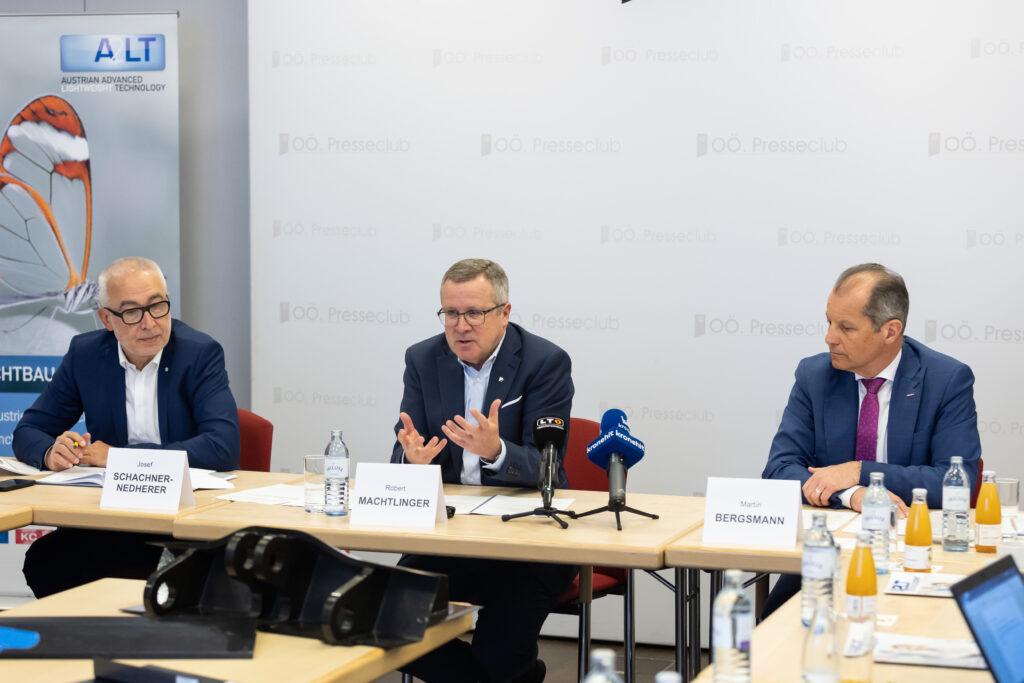 Drei Männer sitzen bei einer Pressekonferenz.