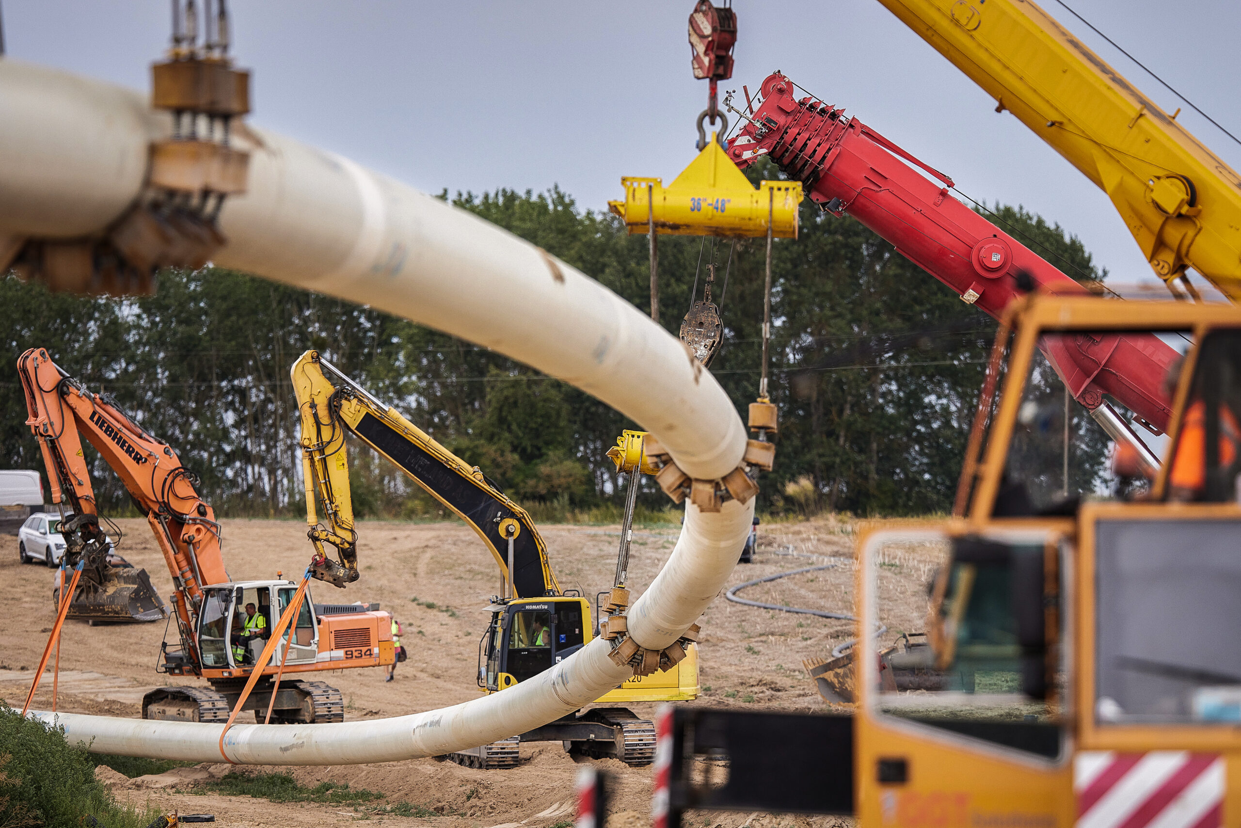 Eine Gaspipeline inmitten einer Baustelle. Rundherum stehen viele Bagger und ein Kran.